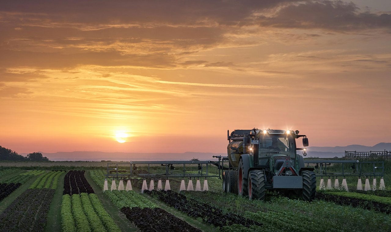 tractor spraying field at sunset