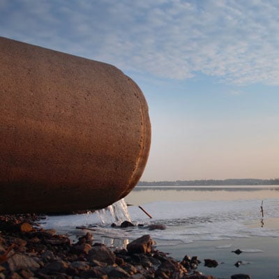 Image: Drainage pipe with process water containing PFAS flowing into a lake