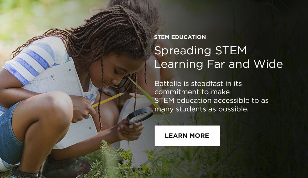 Photo: stem student using magnifying glass to examine plants in a field