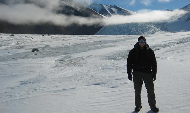 alt=Eric Solok standing in front of a range of mountains in the mcmurdo dry valleys