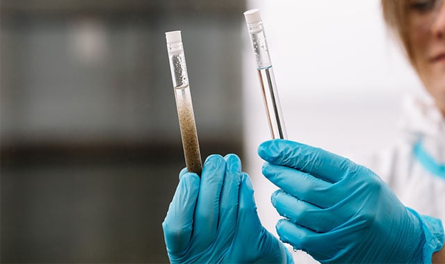 environmental scientist examining test tubes of water, one with noticeably darker water