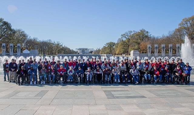 alt= Seventy six veterans stand together at the World War II Memorial during Honor Flight 147 in Washington, D.C.
