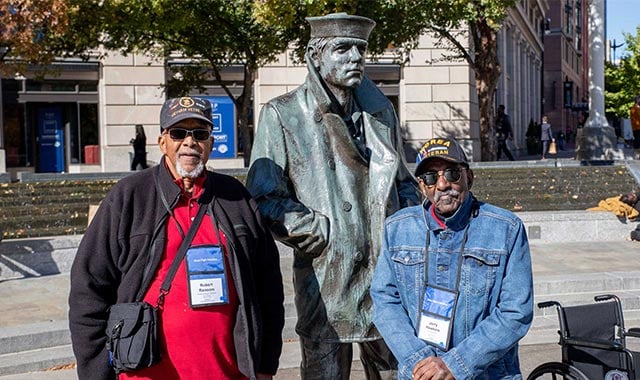 alt= Vietnam War Veteran Robert Ransom stands with Korean War Veteran Jerry Hawkins at the U.S. Navy Memorial with the Lone Sailor statute