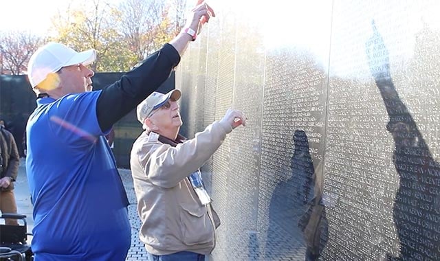 alt= A veteran and his Honor Flight Guardian search for a friends name on the Vietnam War Memorial