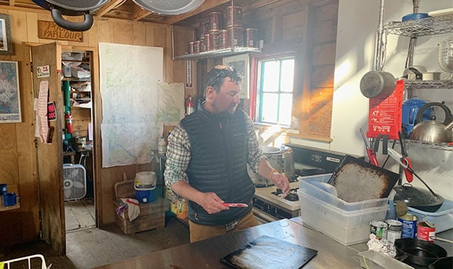 alt=matt zeglen washing dishes in their alaskan hut during their time in jirp