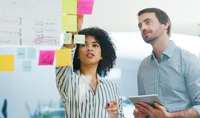 alt=oung businessman and businesswoman using a digital tablet while having a research and development brainstorming session for a new medical device in a modern office