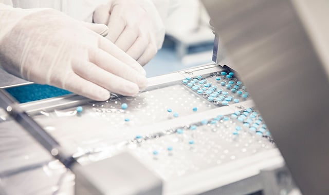 alt= close up of manufacturer placing pills into an assembly line